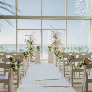 Indoor foyer wedding ceremony with floral aisle and ocean views at Secrets The Vine, Cancun