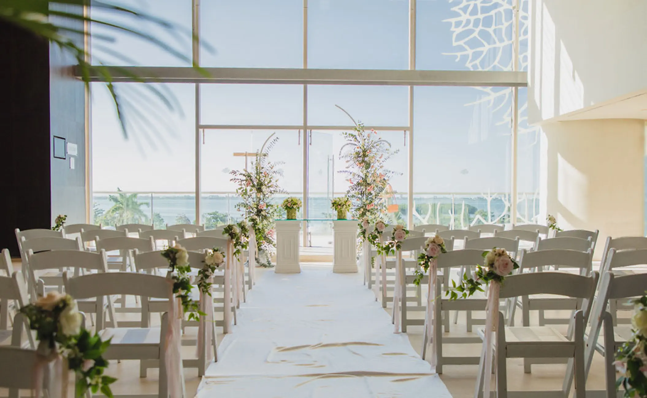 Indoor foyer wedding ceremony with floral aisle and ocean views at Secrets The Vine, Cancun