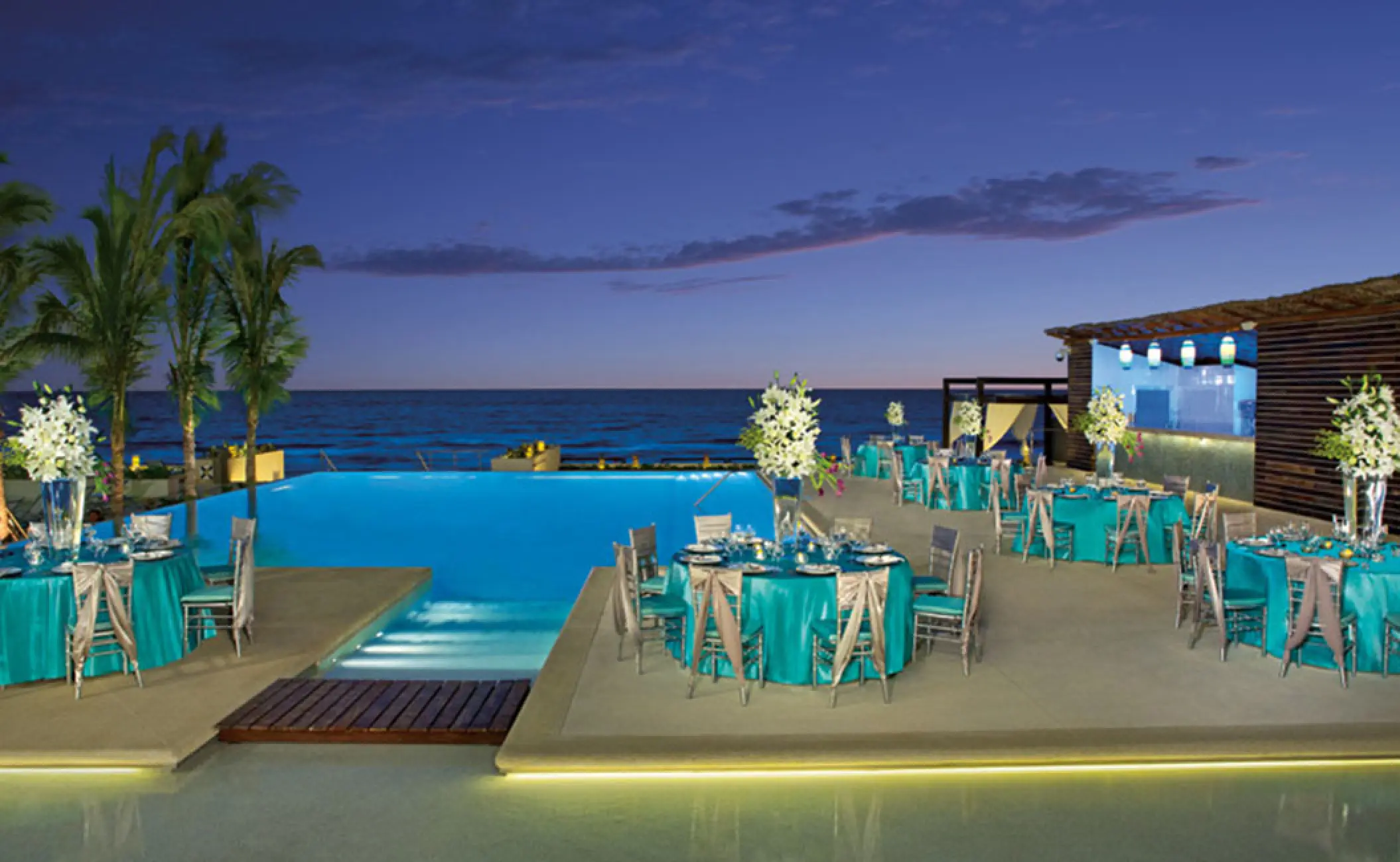 Evening wedding reception with turquoise linens on the pool terrace at Secrets The Vine, Cancun