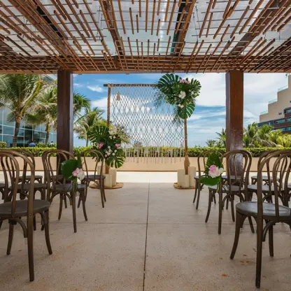 The Vine Lounge terrace wedding ceremony with wooden chairs and tropical floral arch at Secrets The Vine, Cancun