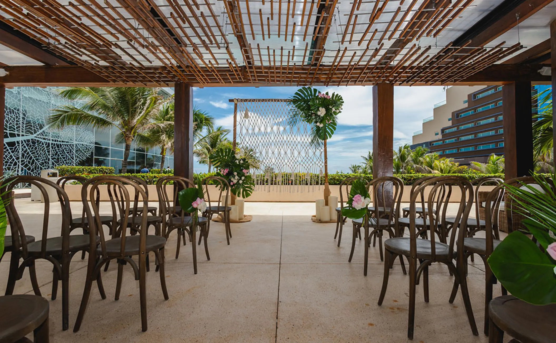 The Vine Lounge terrace wedding ceremony with wooden chairs and tropical floral arch at Secrets The Vine, Cancun
