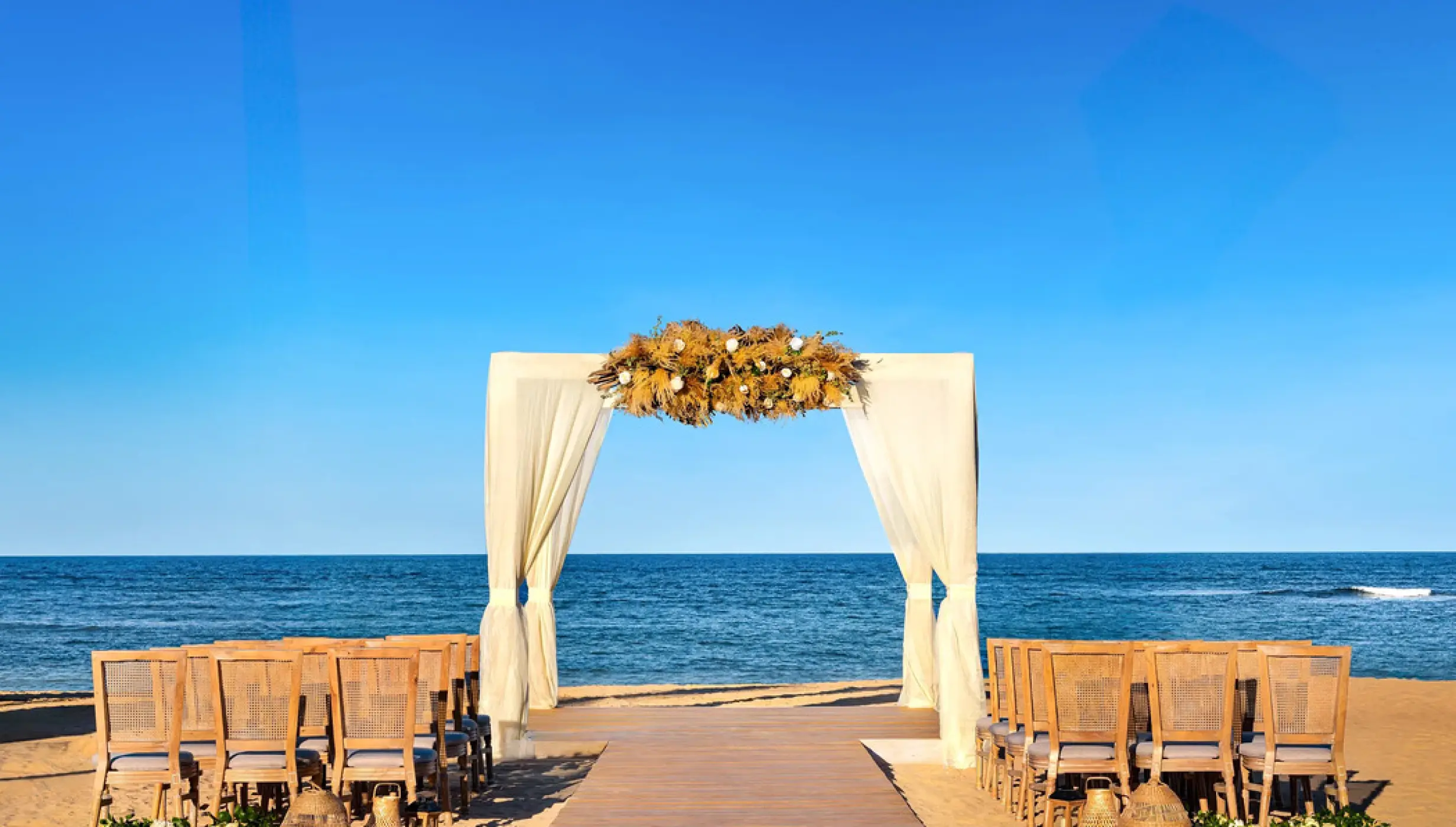 Beachfront wedding ceremony with a white draped arch at Secrets Tides, Punta Cana