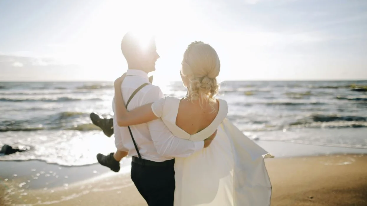 groom carrying bride in his arms on the beach