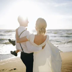 groom carrying bride in his arms on the beach