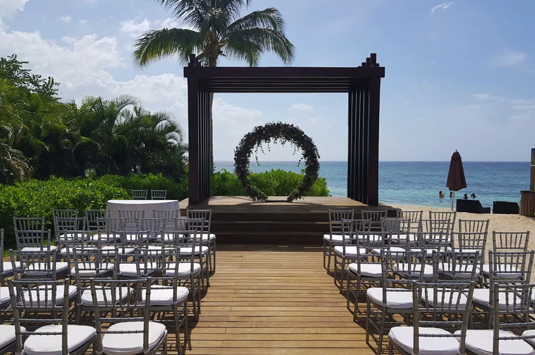 Beachfront wedding ceremony setup with floral hoop arch and silver chairs at Secrets St James, Montego Bay