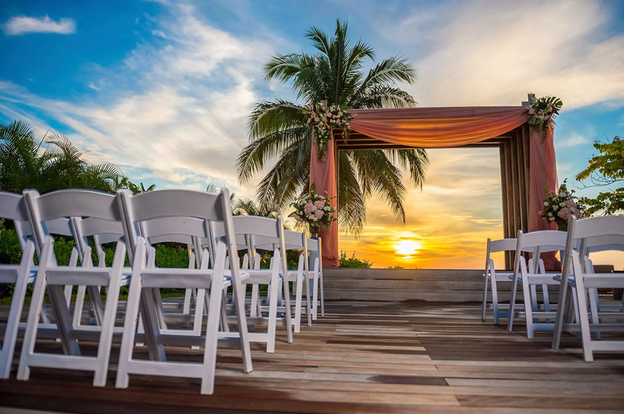 Wooden deck wedding ceremony at sunset with a pink draped arch at Secrets Wild Orchid, Montego Bay