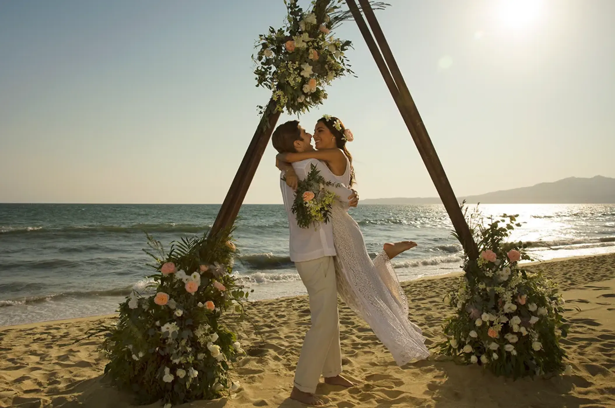 Groom lifting bride in front of a triangle floral arch at Secrets Wild Orchid, Montego Bay