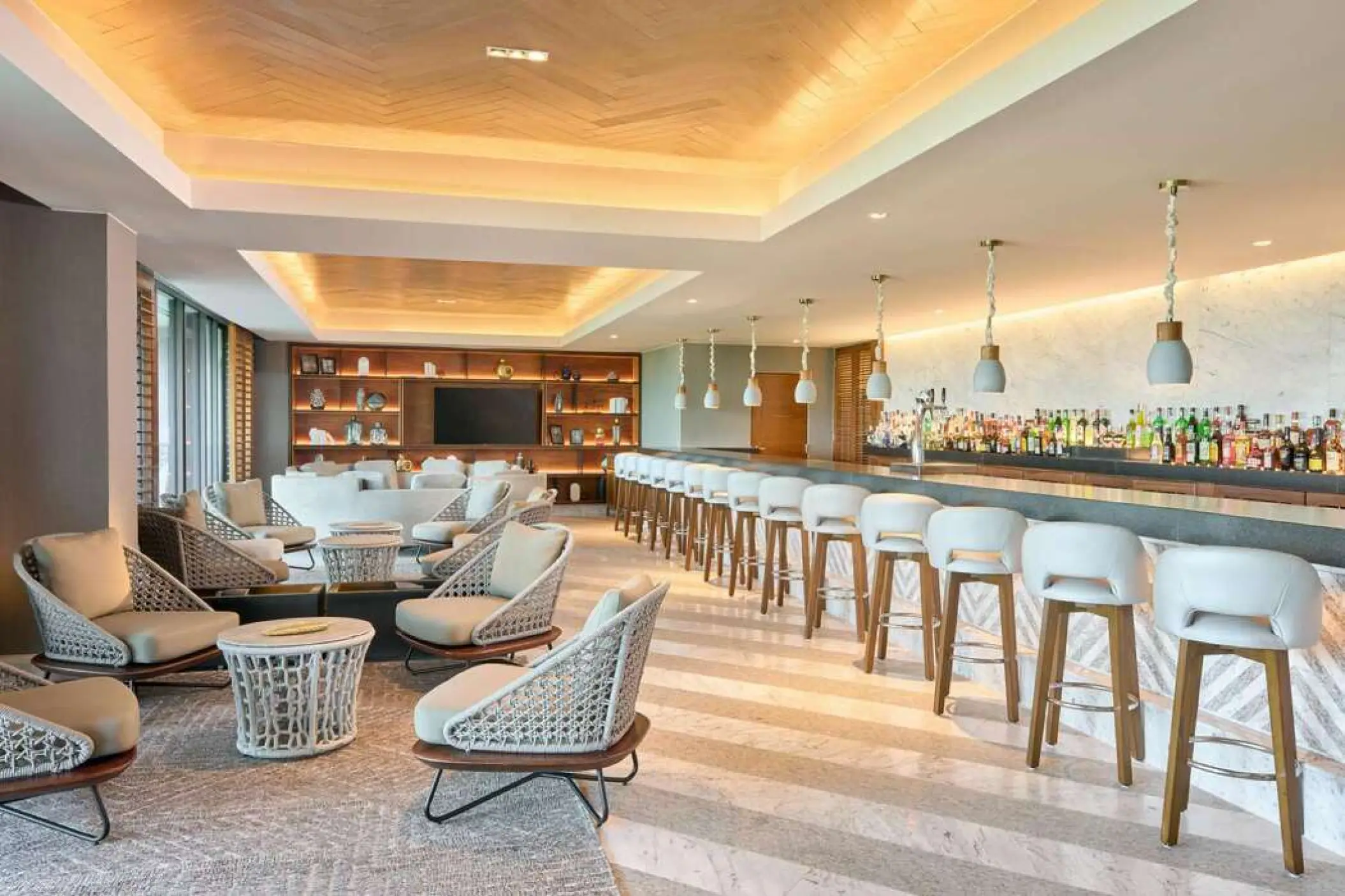 Indoor bar with white barstools and wicker lounge seating at SLS Playa Mujeres, Cancun
