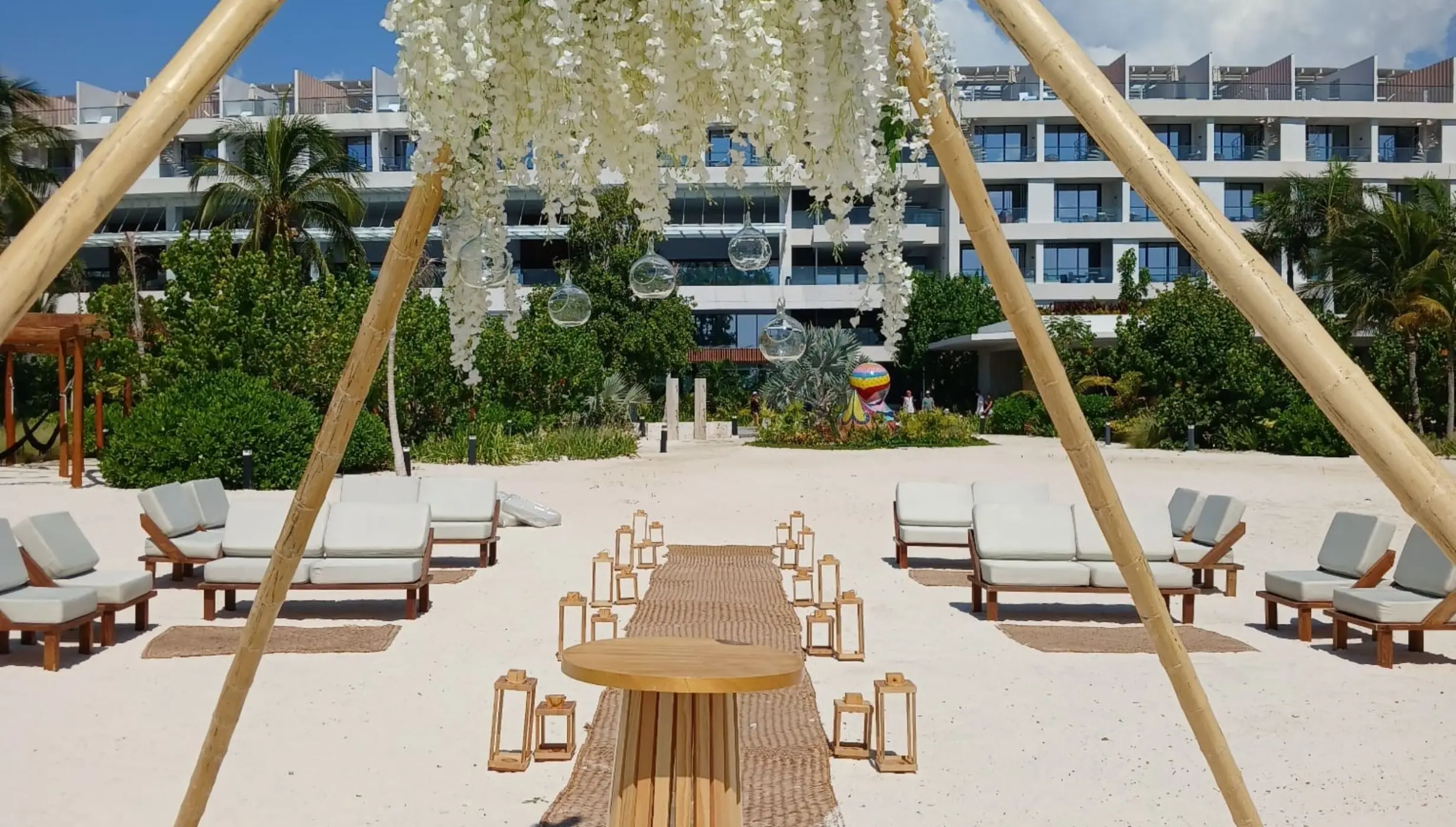 Beach wedding ceremony with a white floral canopy and bamboo structure at SLS Playa Mujeres, Cancun