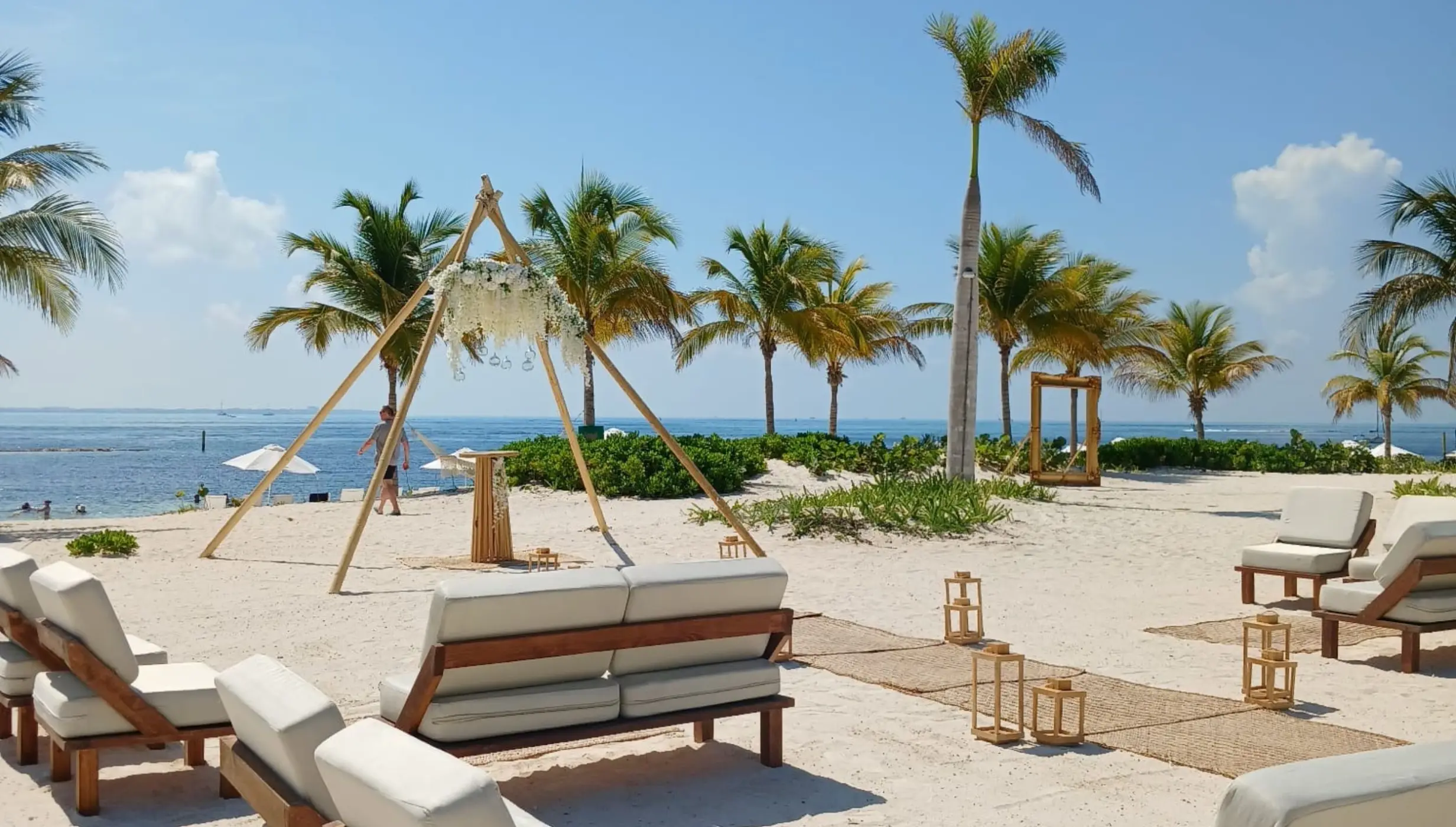 Beachfront wedding ceremony with a triangular arch and lounge seating at SLS Playa Mujeres, Cancun