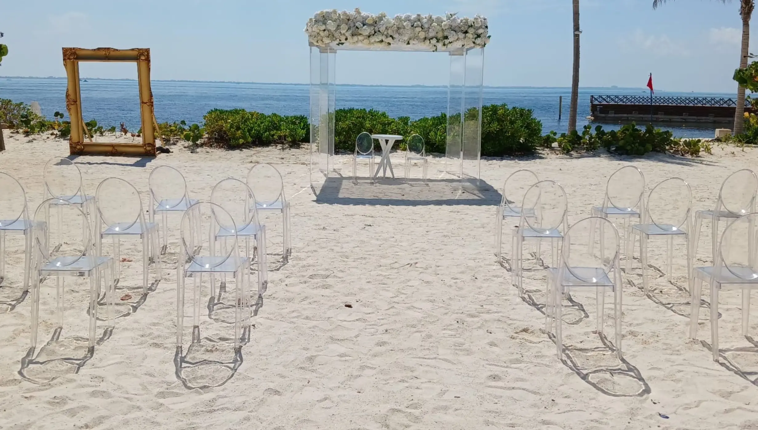 Beachfront wedding ceremony with clear acrylic chairs and a floral arch at SLS Playa Mujeres, Cancun