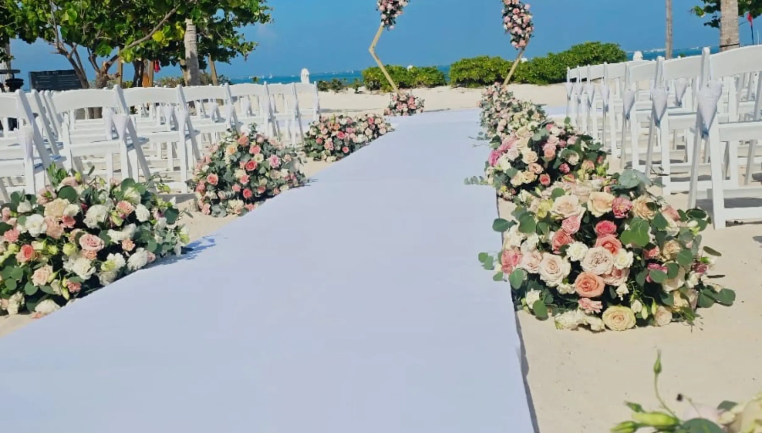 Beachfront wedding ceremony with white runner and floral arrangements at SLS Playa Mujeres, Cancun