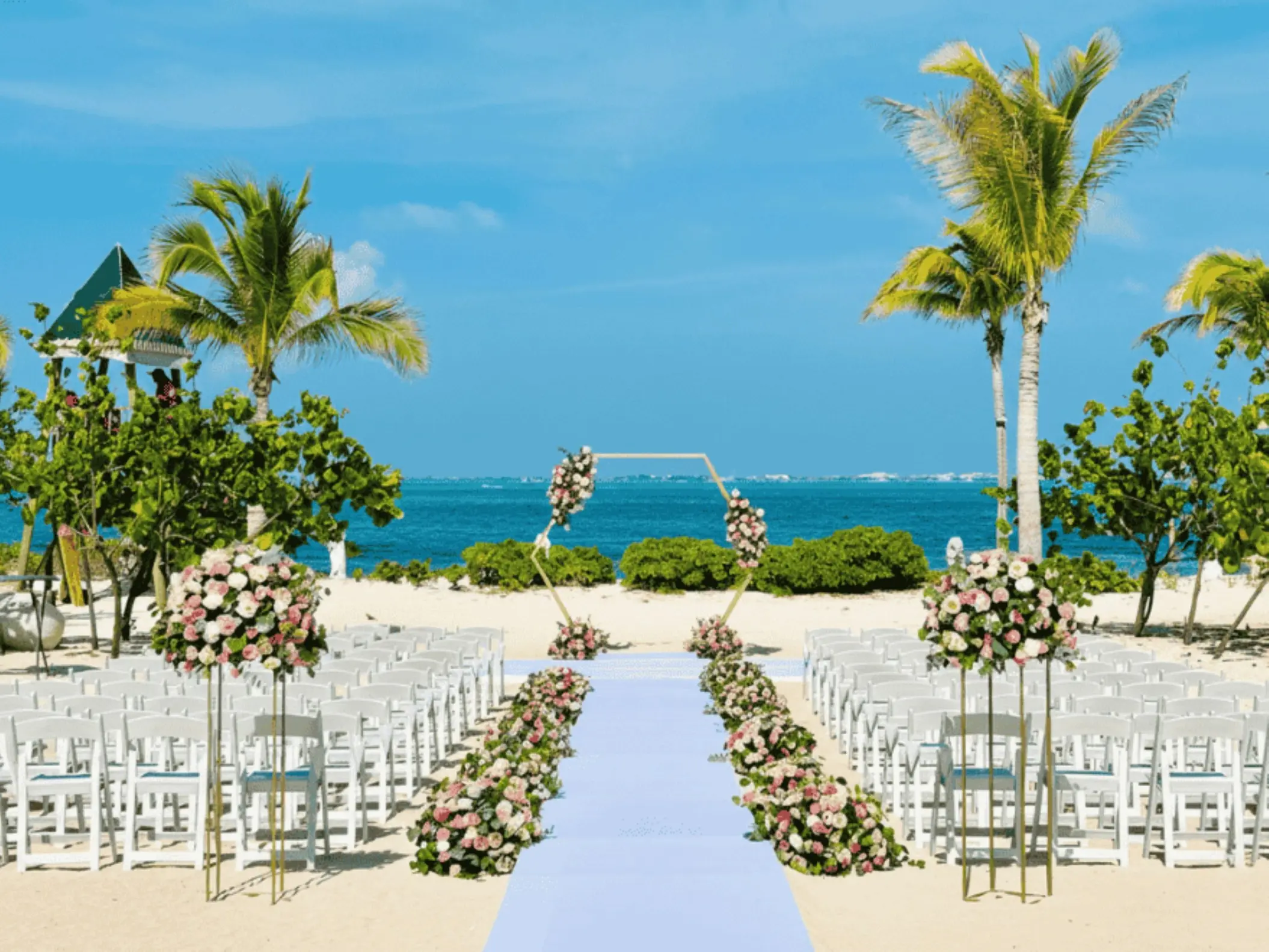 Beachfront wedding ceremony with a floral hexagonal arch and white chairs at SLS Playa Mujeres, Cancun