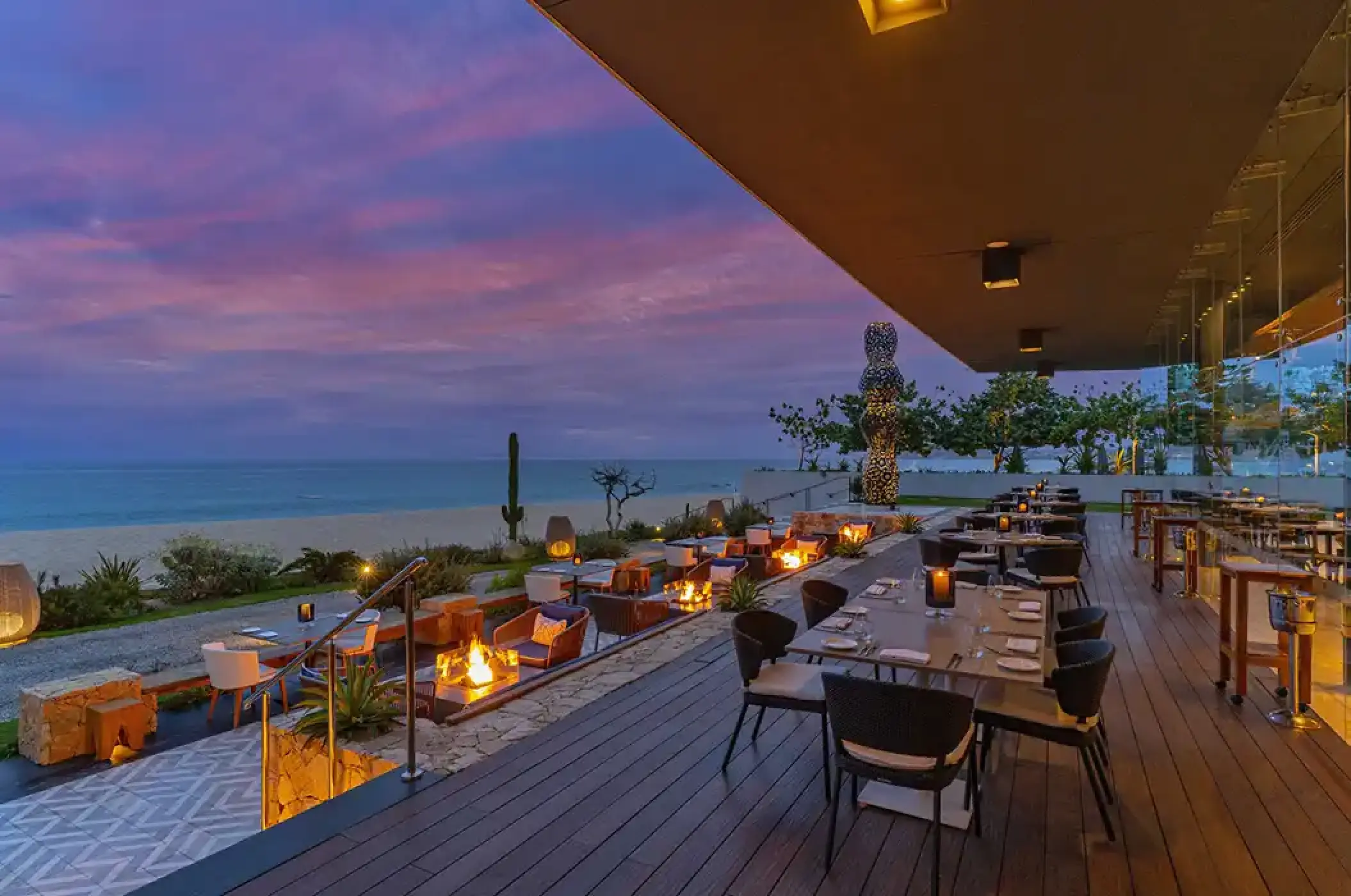 Outdoor terrace at Solaz Los Cabos restaurant with fire pits and beachfront views at sunset, Cabo San Lucas