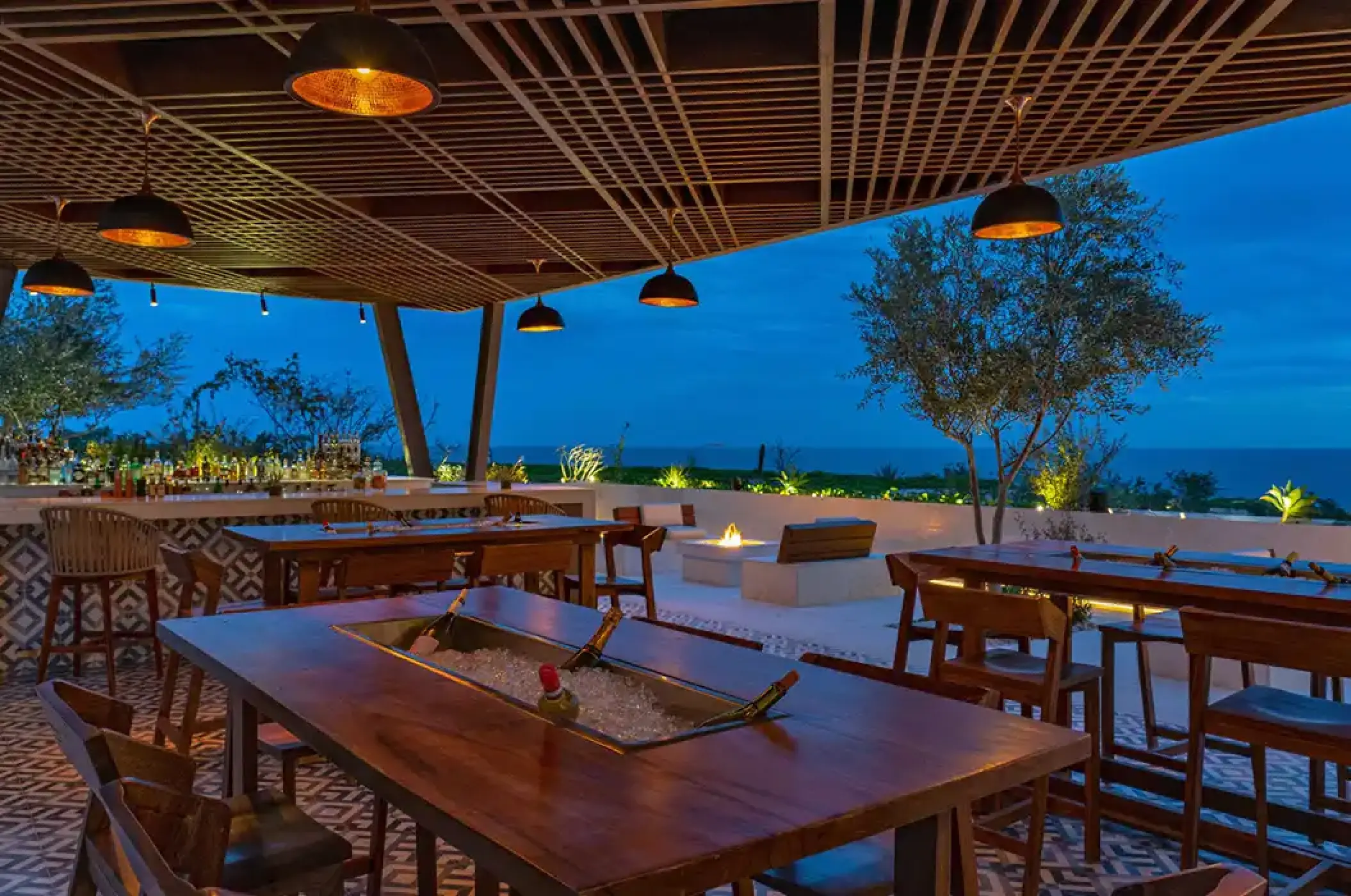 Outdoor bar and lounge with wooden high tables at Solaz Los Cabos, Cabo San Lucas