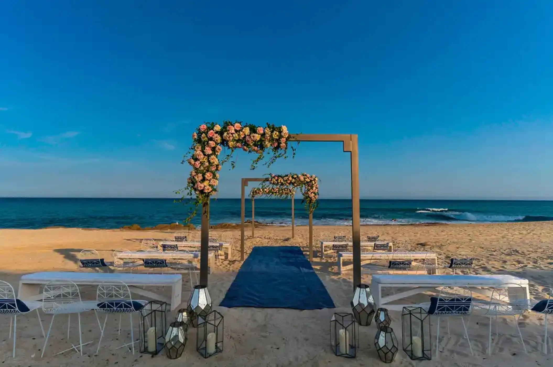 Beachfront wedding ceremony with floral arches and blue aisle runner at Solaz Los Cabos, Cabo San Lucas