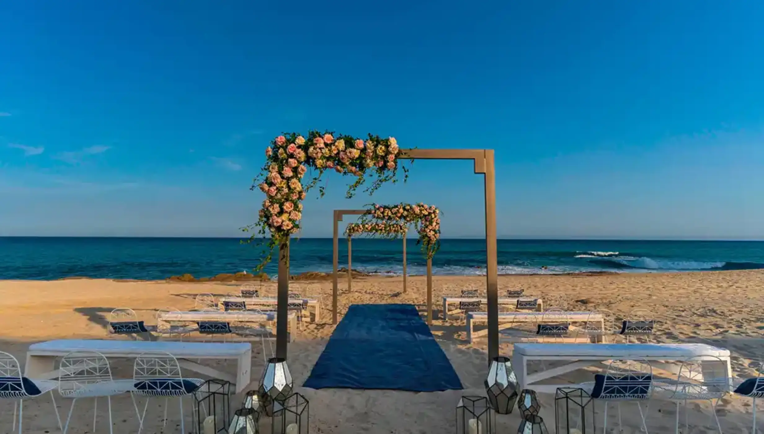 Beachfront wedding ceremony with floral arches and blue aisle runner at Solaz Los Cabos, Cabo San Lucas