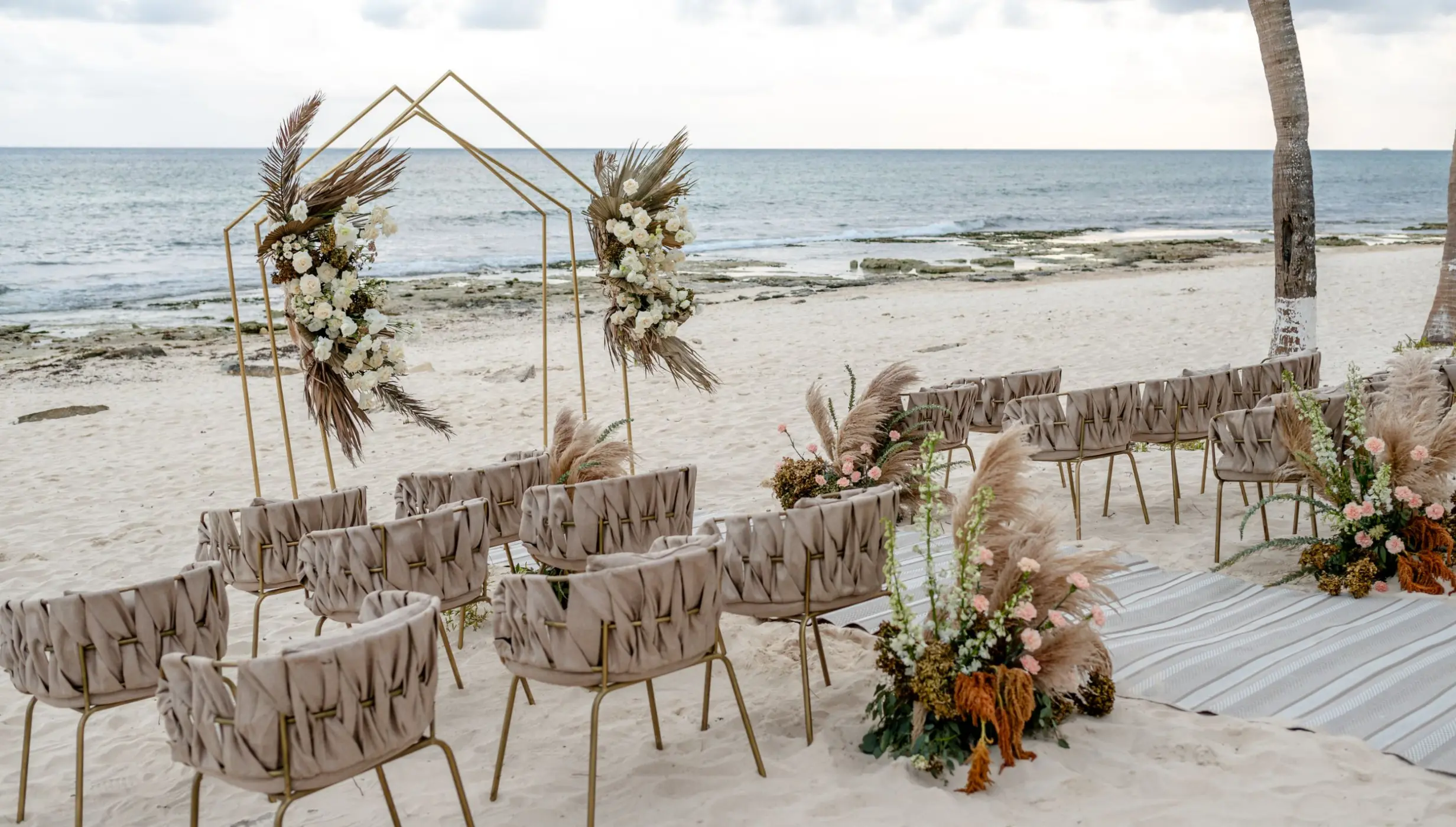 Beachfront wedding ceremony with a gold arch and pampas grass at The Beachfront by The Fives, Playa Del Carmen
