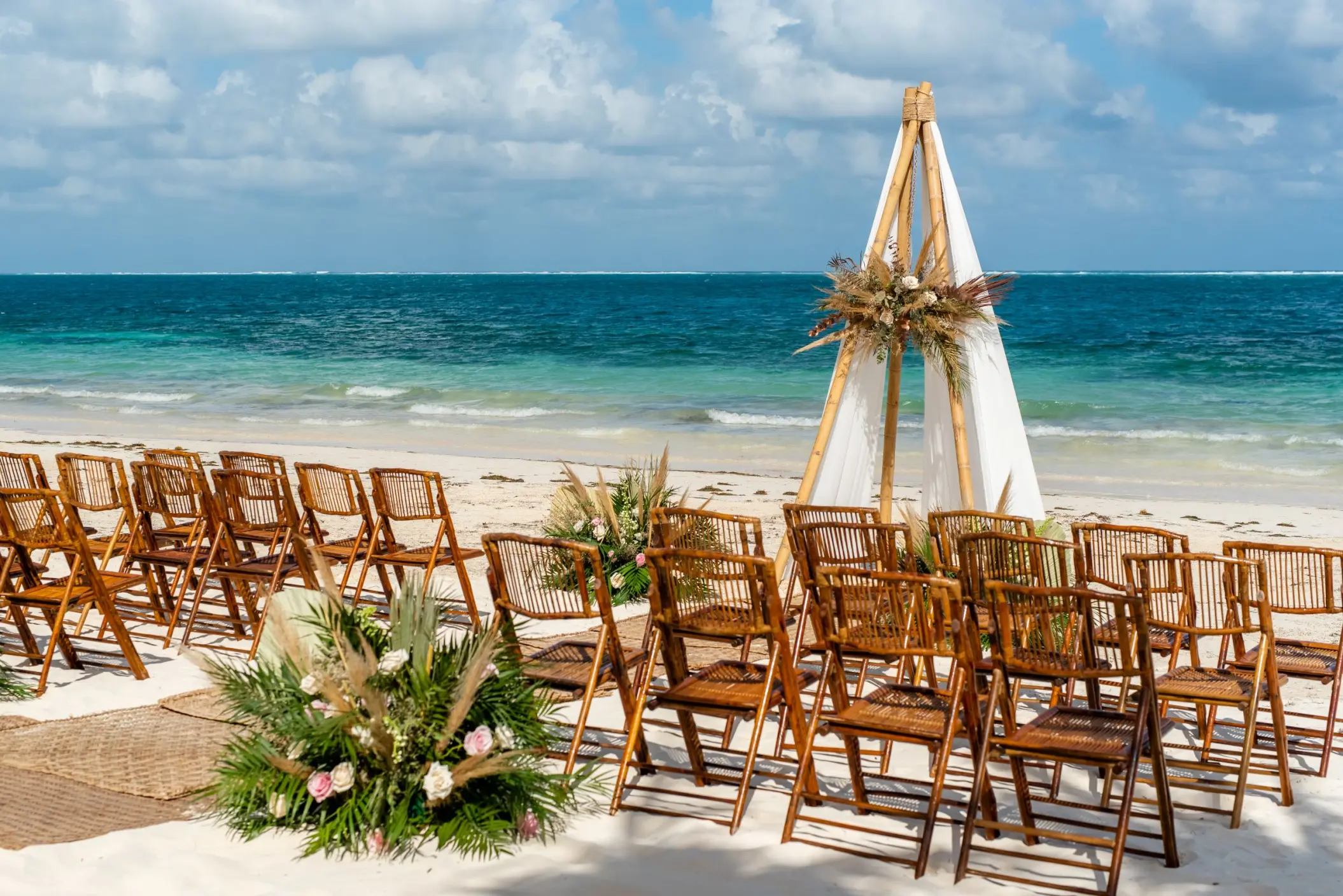 Beachfront wedding ceremony with a teepee arch and wooden chairs at The Fives Oceanfront, Riviera Maya
