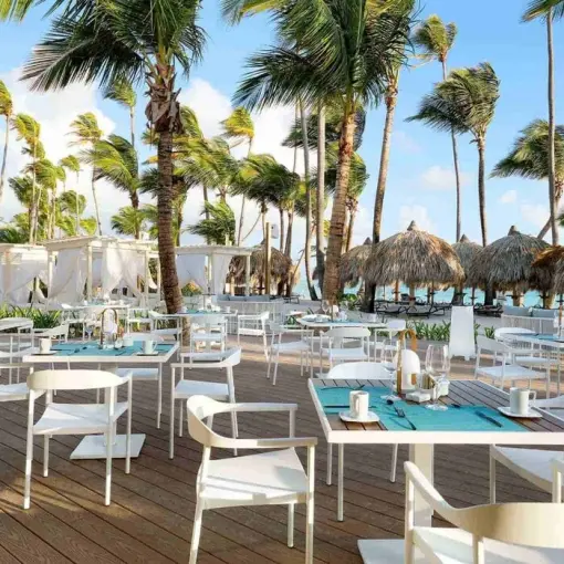 Outdoor beachside restaurant terrace with white tables and palm trees at TRS Turquesa, Punta Cana