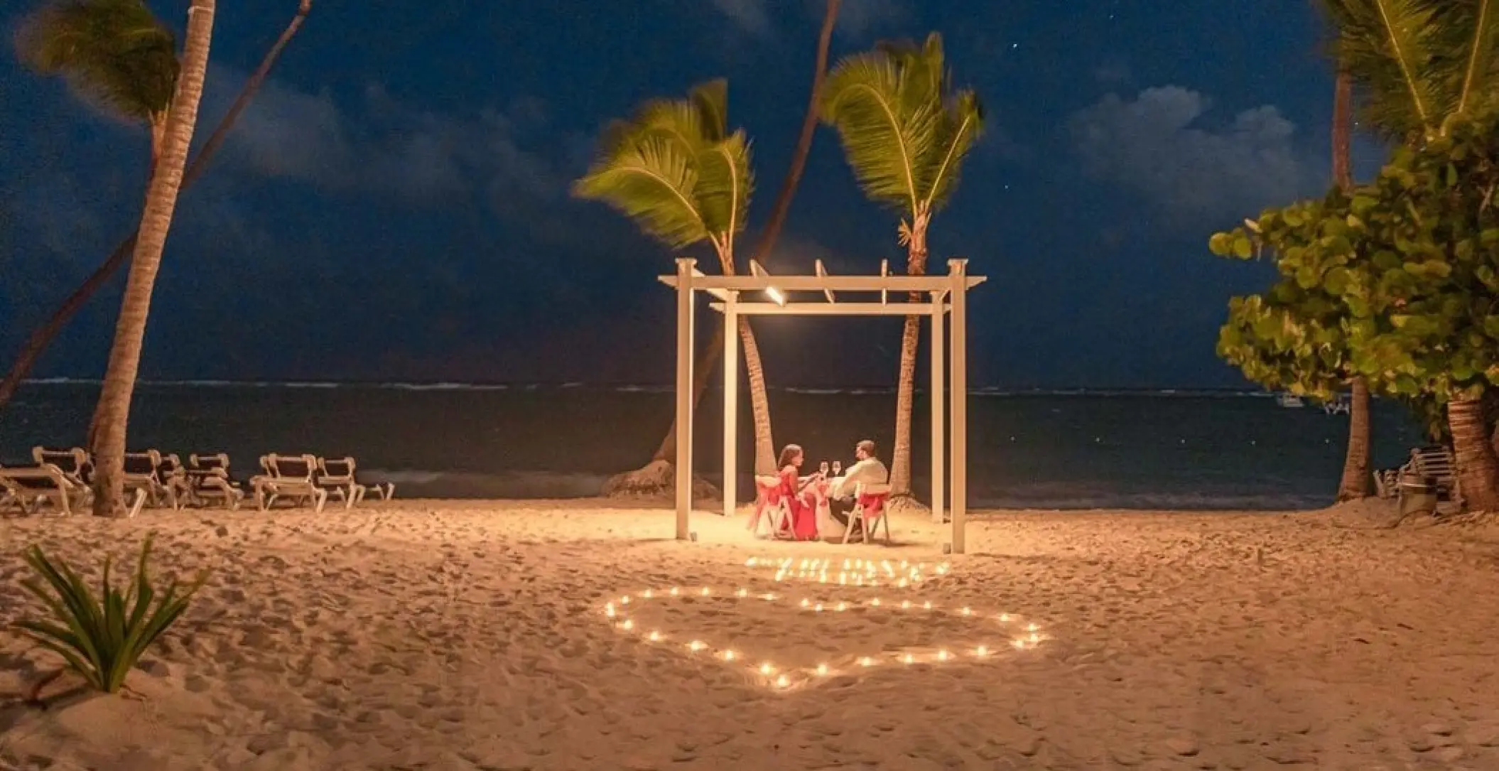 Couple having a private beach dinner under a lit pergola at TRS Turquesa, Punta Cana