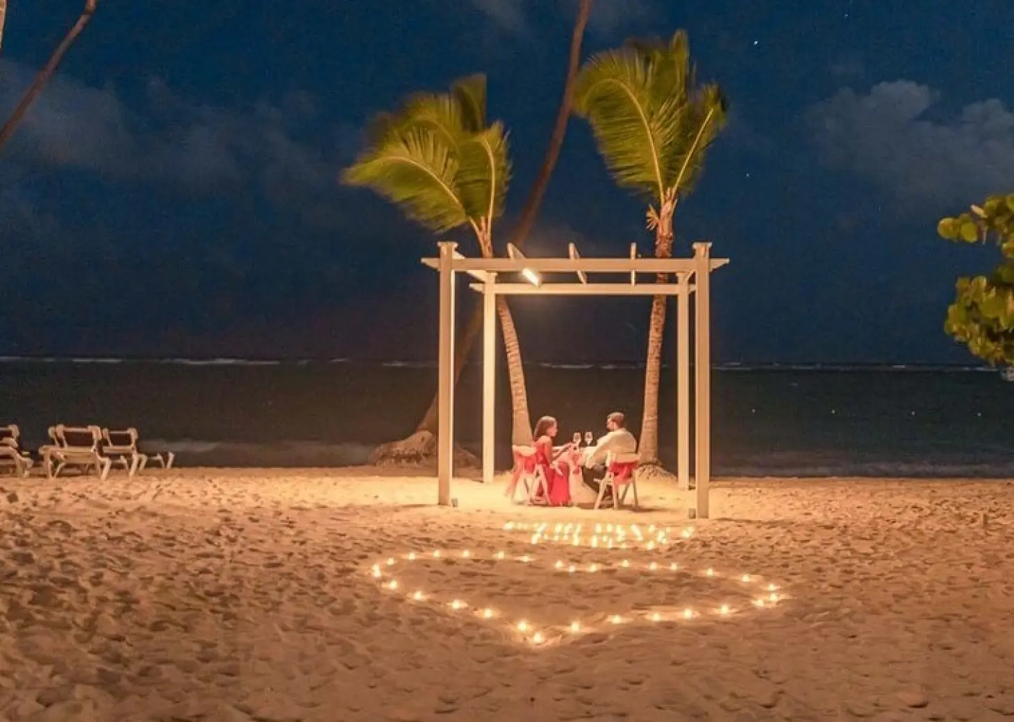 Couple having a private beach dinner under a lit pergola at TRS Turquesa, Punta Cana