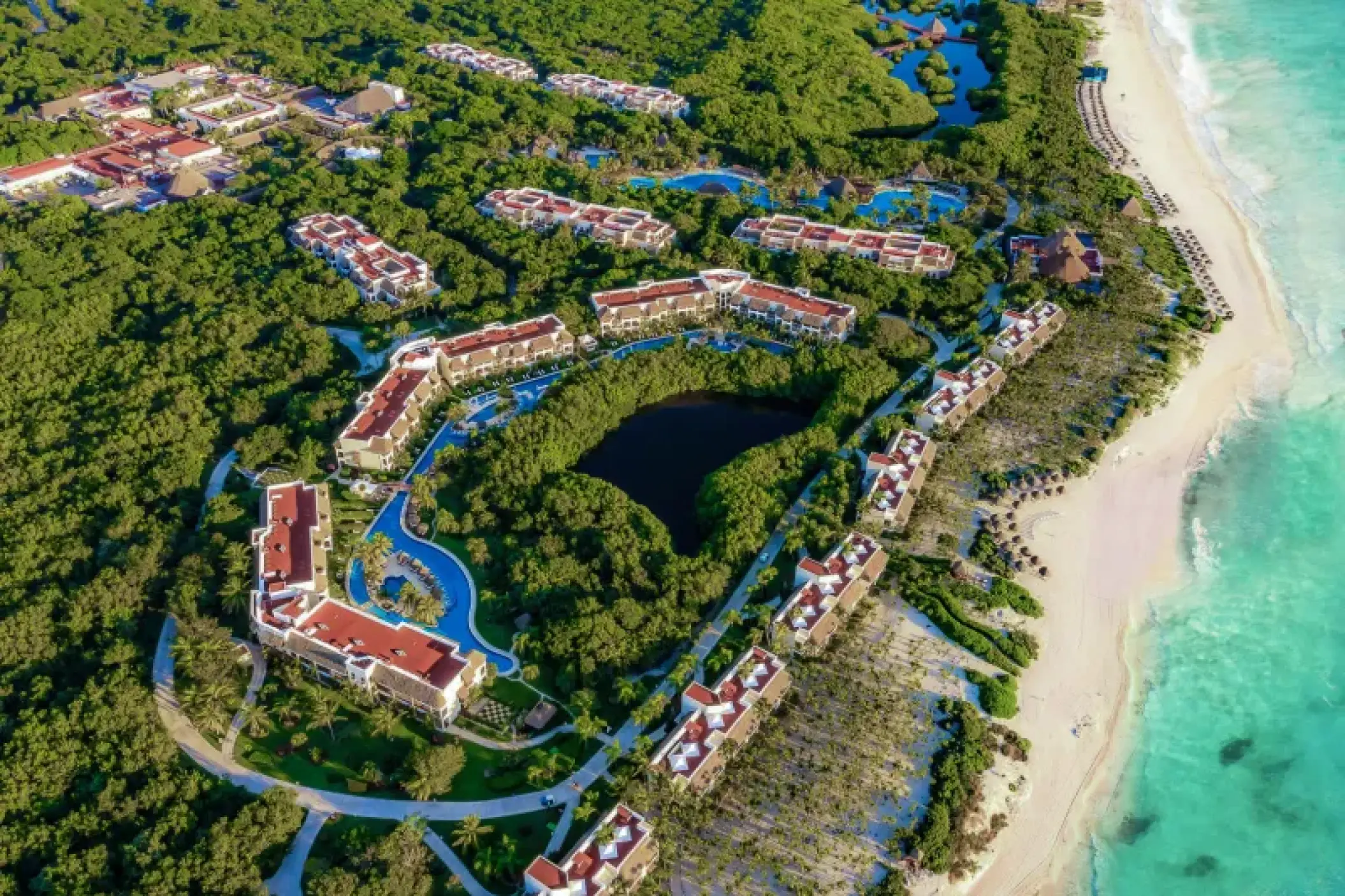 Aerial view of Valentin Imperial Riviera Maya buildings, pools, and lush jungle greenery by the beach