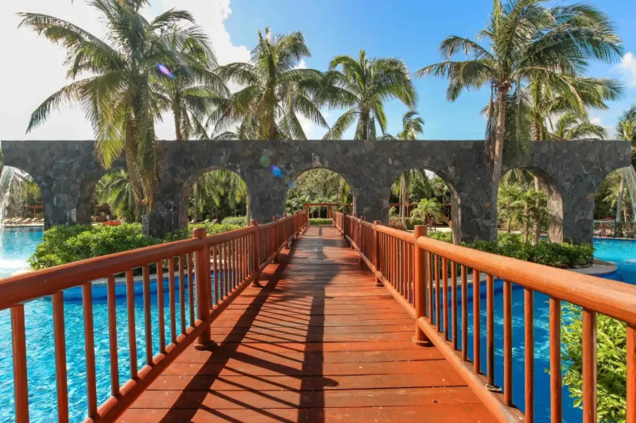 Wooden bridge leading through stone arches over the swimming pool at Valentin Imperial, Riviera Maya