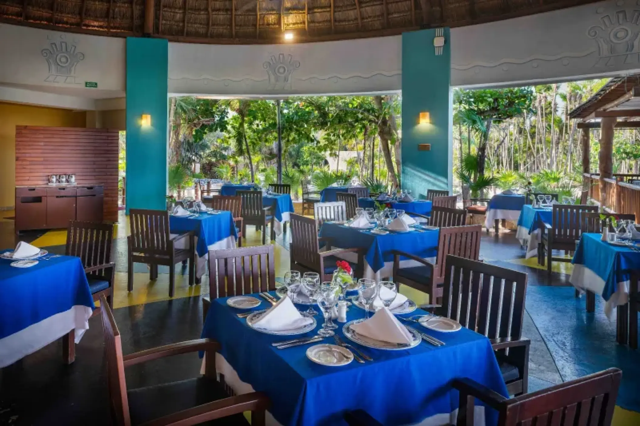 Indoor restaurant with blue tablecloths and views of tropical gardens at Valentin Imperial, Riviera Maya