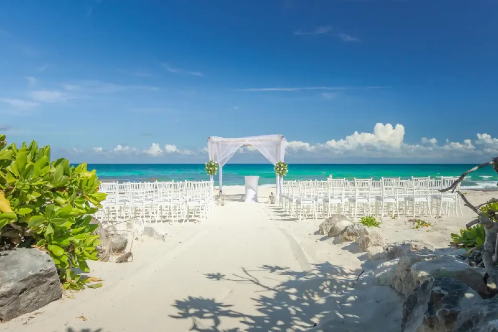 Beachfront wedding ceremony with white huppah and chairs at Valentin Imperial, Riviera Maya