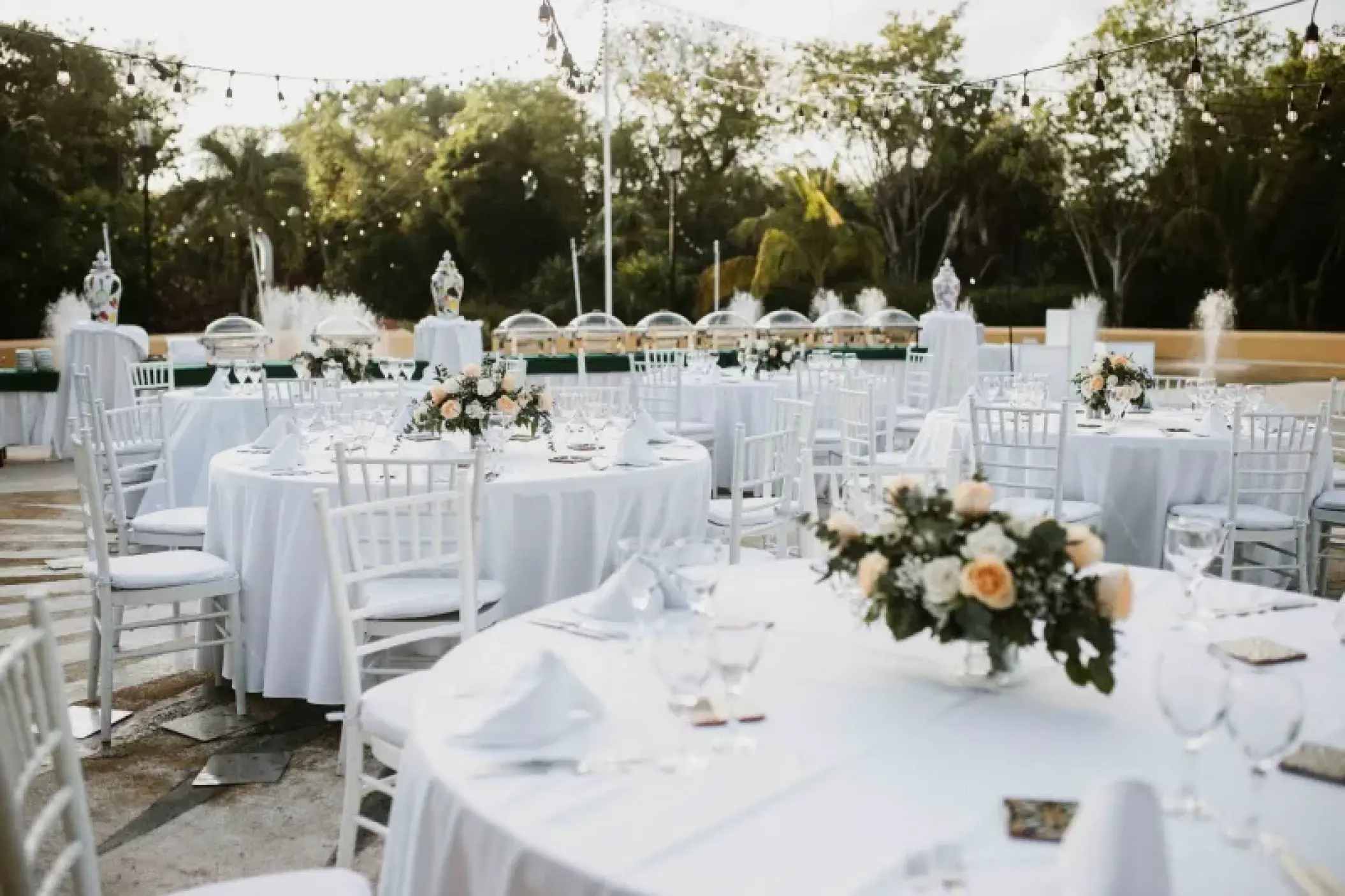Outdoor wedding reception with white tables, floral centerpieces, and string lights at Valentin Imperial, Riviera Maya