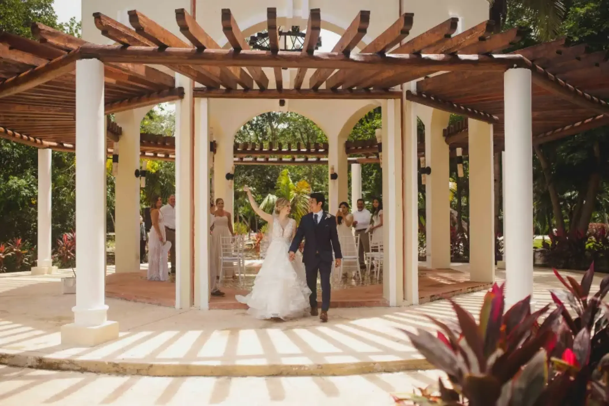 Bride and groom walking through a garden gazebo wedding ceremony at Valentin Imperial, Riviera Maya