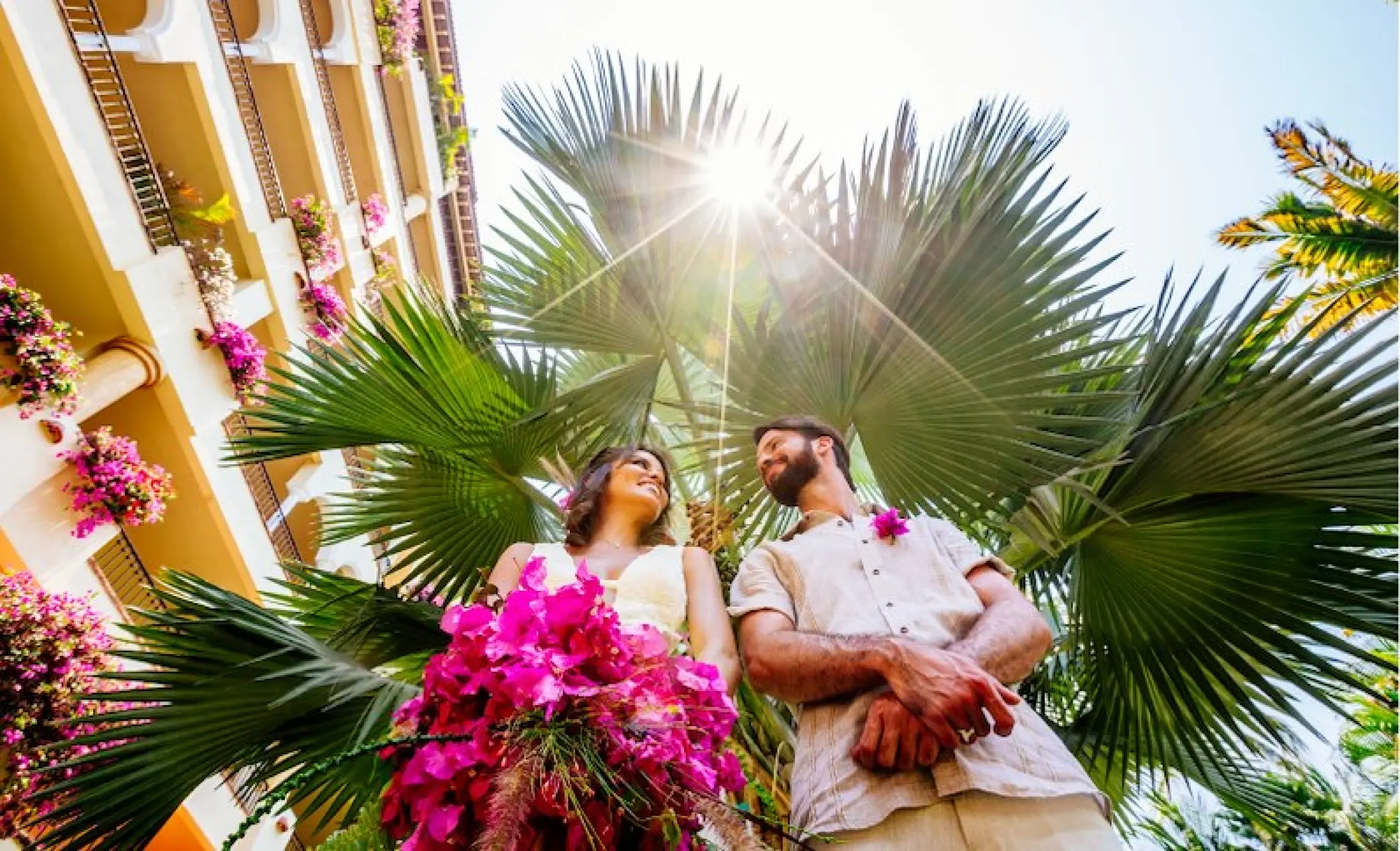 Low-angle portrait of a bride and groom under palm trees at Velas Vallarta, Puerto Vallarta