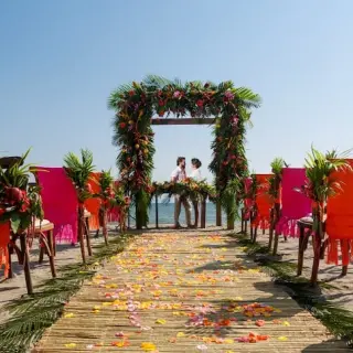 Beachfront wedding ceremony with a floral arch and colorful chairs at Velas Vallarta, Puerto Vallarta