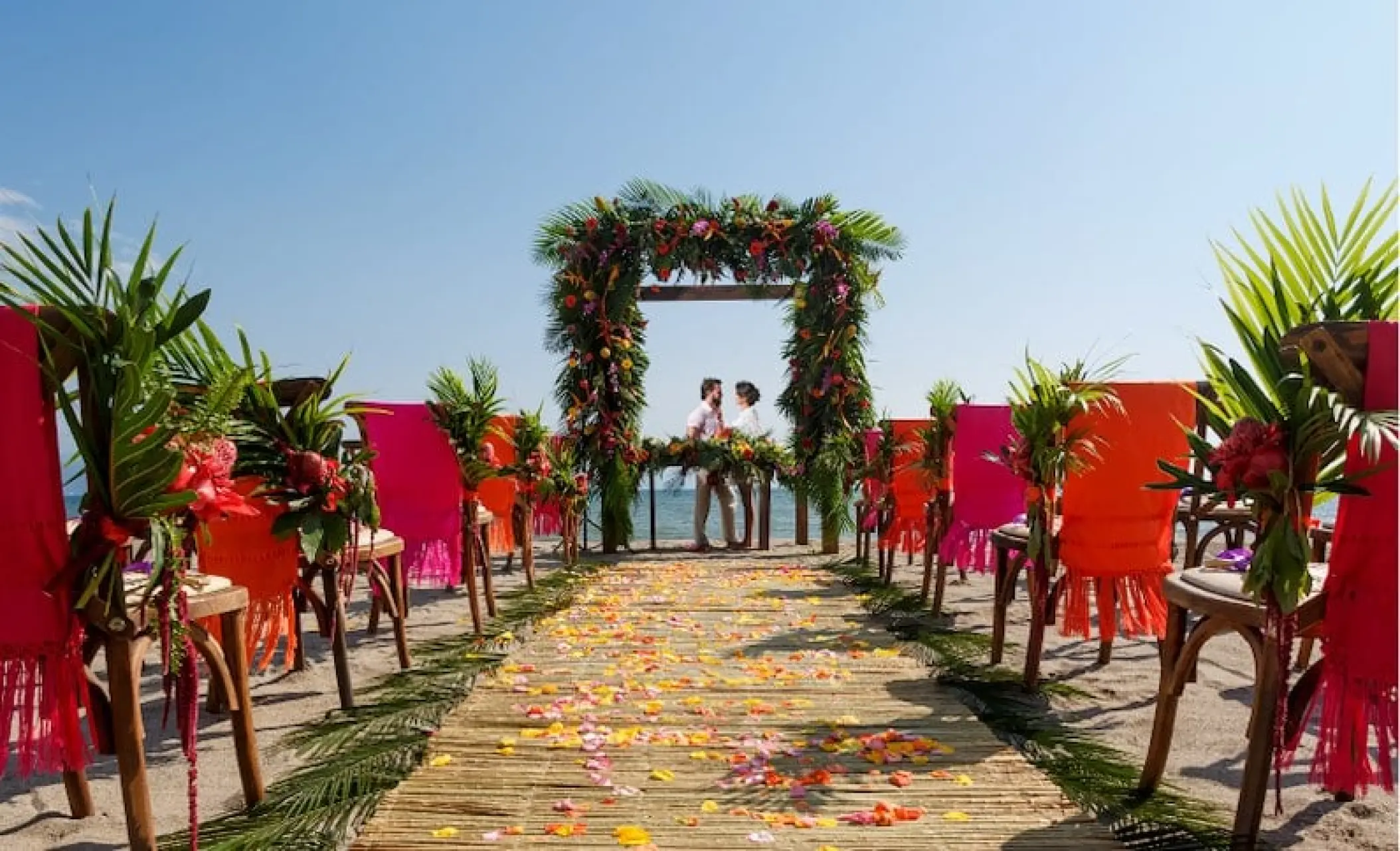 Beachfront wedding ceremony with a floral arch and colorful chairs at Velas Vallarta, Puerto Vallarta