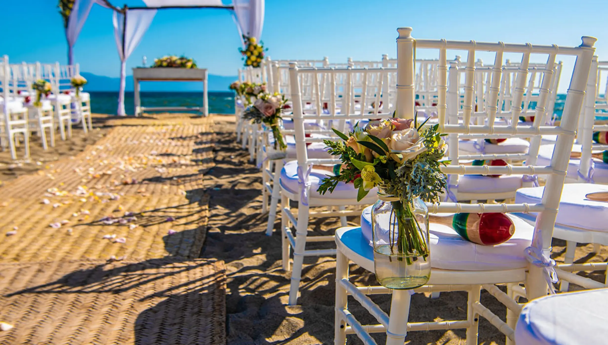 Beachfront wedding ceremony with white chairs and floral accents at Velas Vallarta, Puerto Vallarta