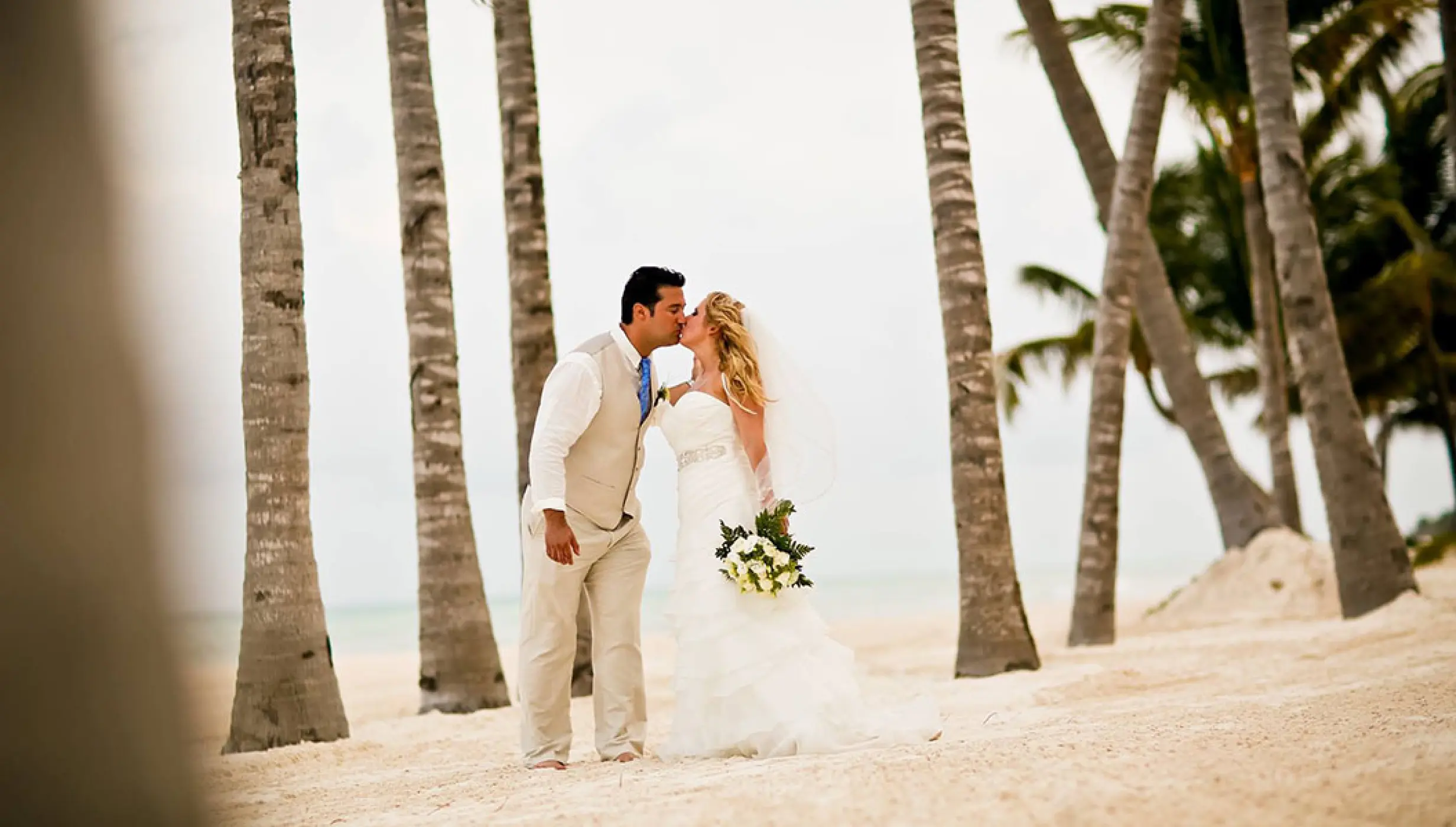 Bride and groom kissing on the beach among palm trees at Velas Vallarta, Puerto Vallarta