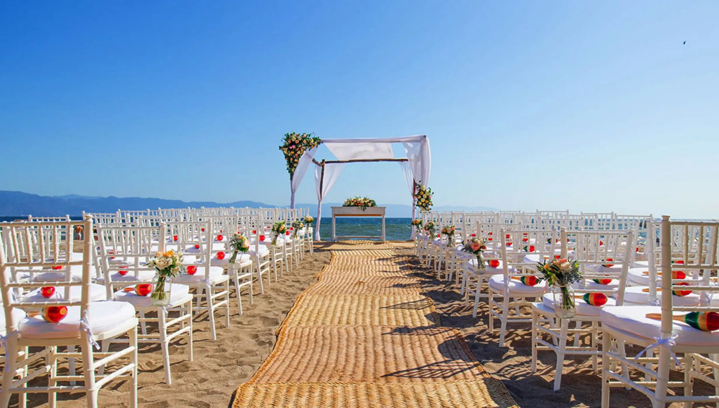 Beachfront wedding ceremony with white chairs and floral arch at Velas Vallarta, Puerto Vallarta
