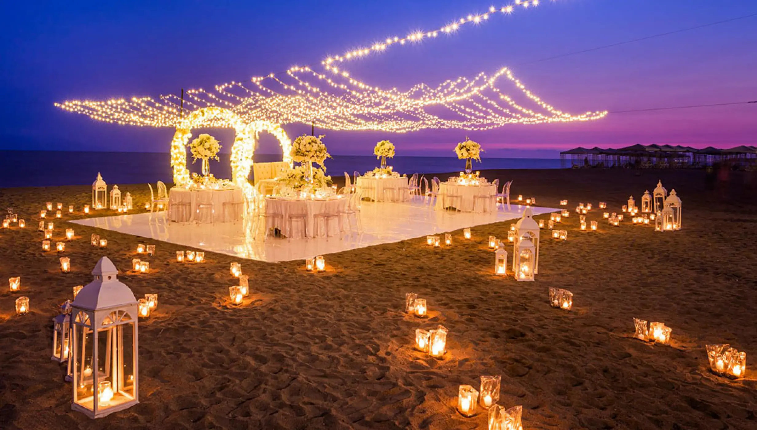 Outdoor wedding reception at Velas Vallarta, Puerto Vallarta with string lights and lanterns on the beach at dusk