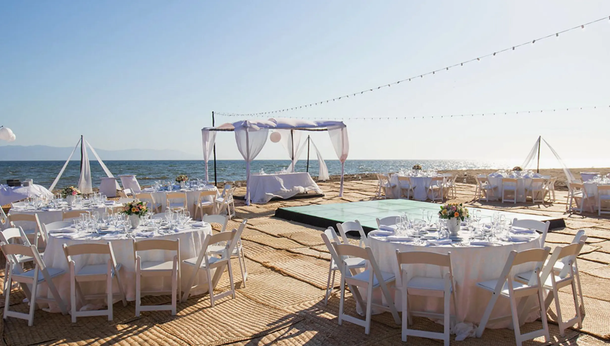 Beachfront wedding reception setup with white tables and a dance floor at Velas Vallarta, Puerto Vallarta