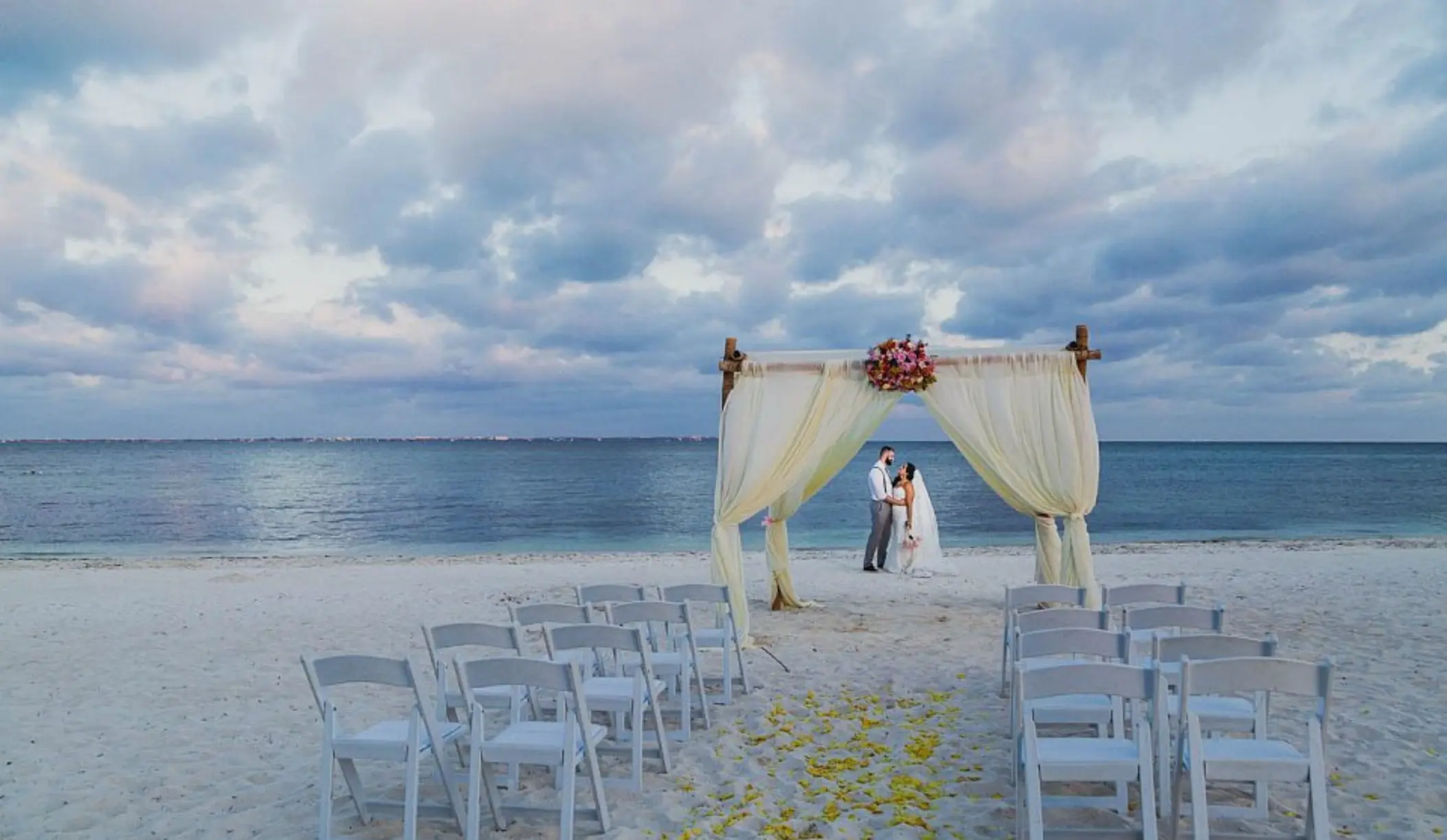 Beach ceremony venue at Villa del Palmar Cancun with a couple standing under a draped bamboo arch