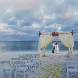 Beach ceremony venue at Villa del Palmar Cancun with a couple standing under a draped bamboo arch
