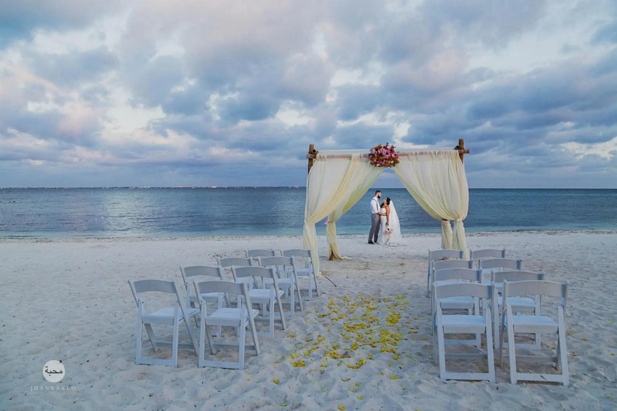 Beachfront wedding ceremony with a white fabric arch and the couple at Villa del Palmar, Cancun