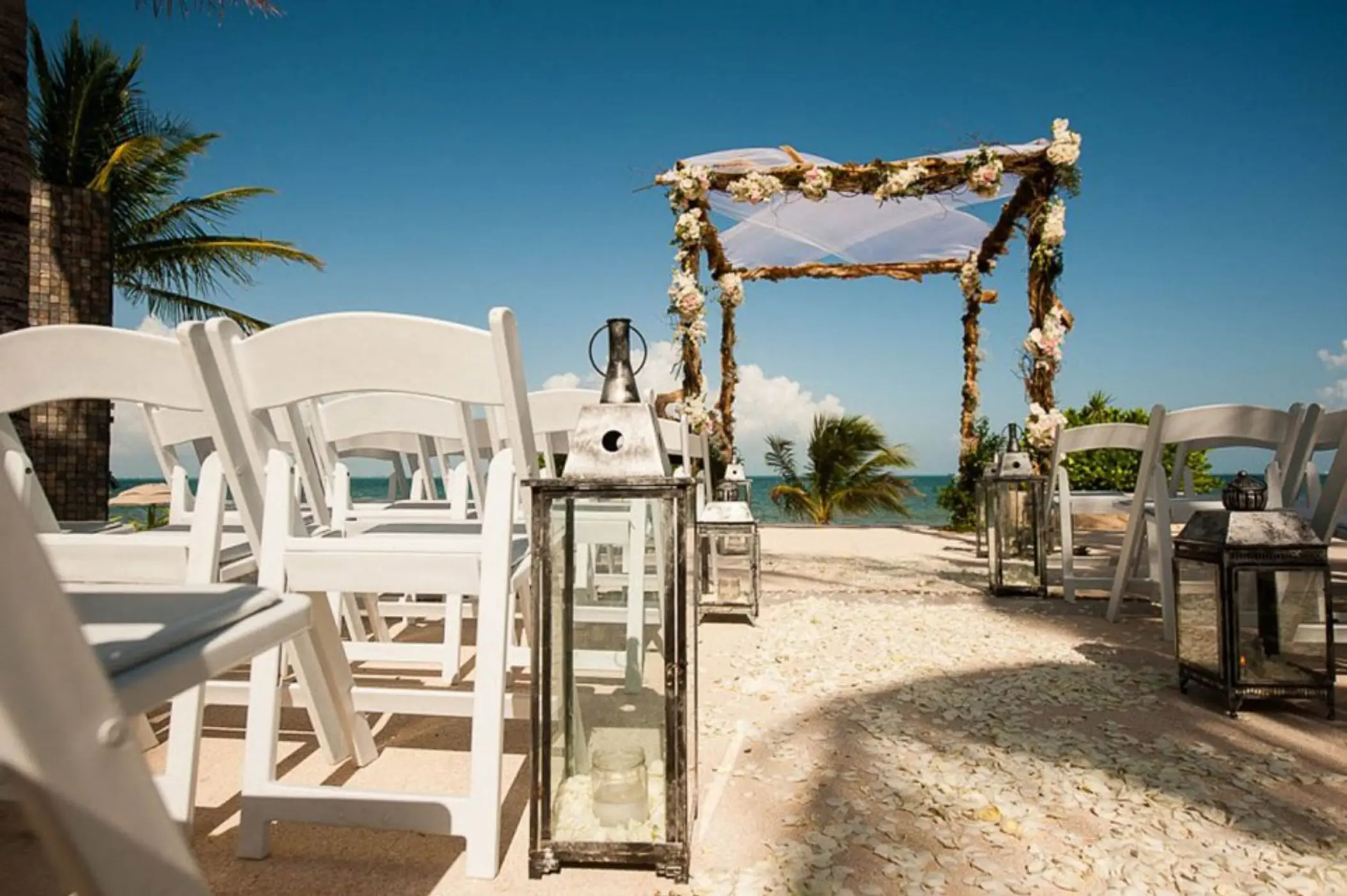 Beachfront wedding ceremony setup with white chairs and a floral arch at Villa del Palmar, Cancun