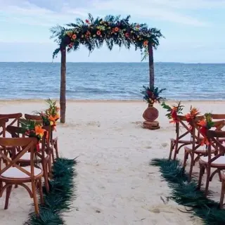 Beachfront wedding ceremony with a floral wooden arch and cross-back chairs at Villa del Palmar Cancun