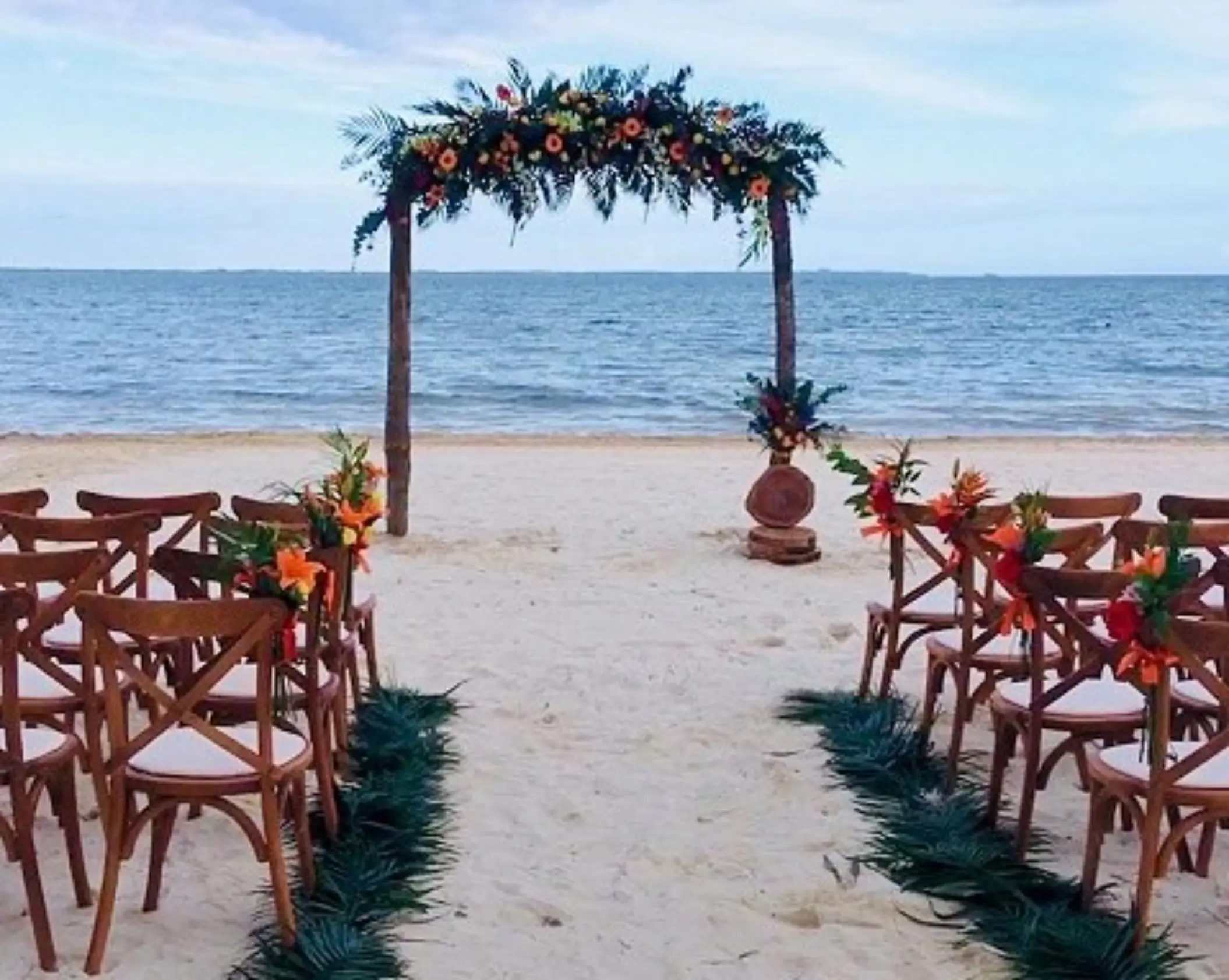 Beachfront wedding ceremony with a floral wooden arch and cross-back chairs at Villa del Palmar Cancun