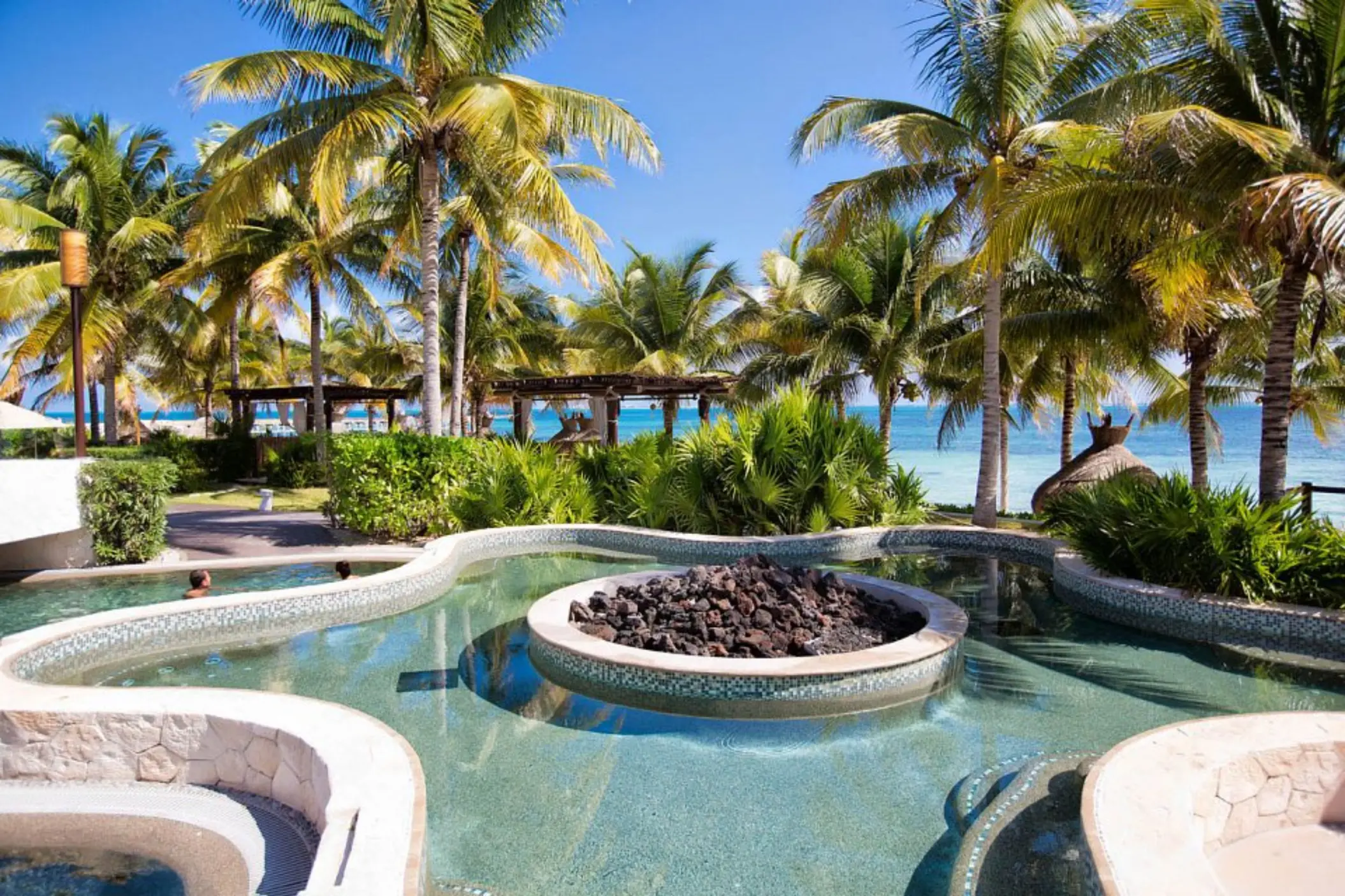 Outdoor hot tub with central fire pit surrounded by palm trees at Villa del Palmar, Cancun