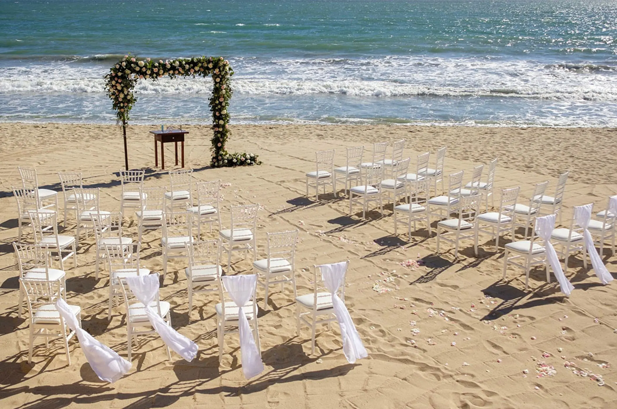 Beachfront wedding ceremony with white chairs and floral arch at Villa La Estancia, Puerto Vallarta