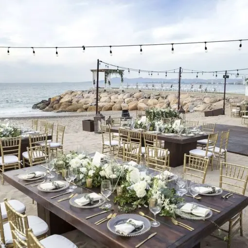 Beachfront wedding reception at Villa Premiere, Puerto Vallarta with wooden tables, gold chairs, and string lights
