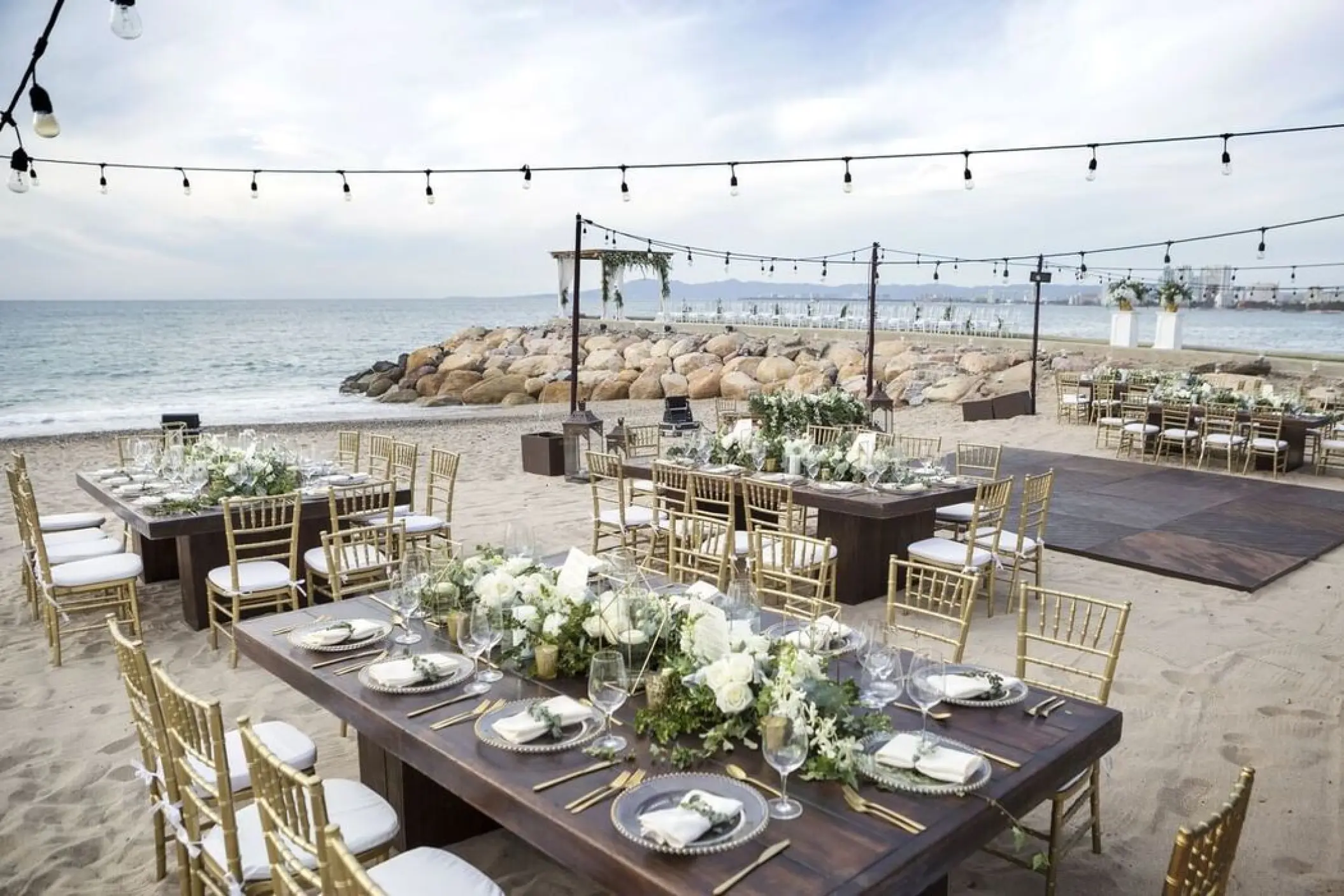 Beachfront wedding reception at Villa Premiere, Puerto Vallarta with wooden tables, gold chairs, and string lights